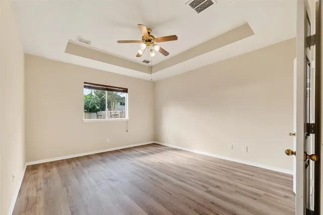 an empty room with wooden floor chandelier fan and windows