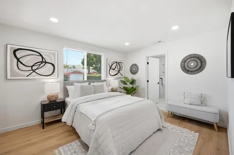 a bedroom with a bed and a lamp on dresser with wooden floor
