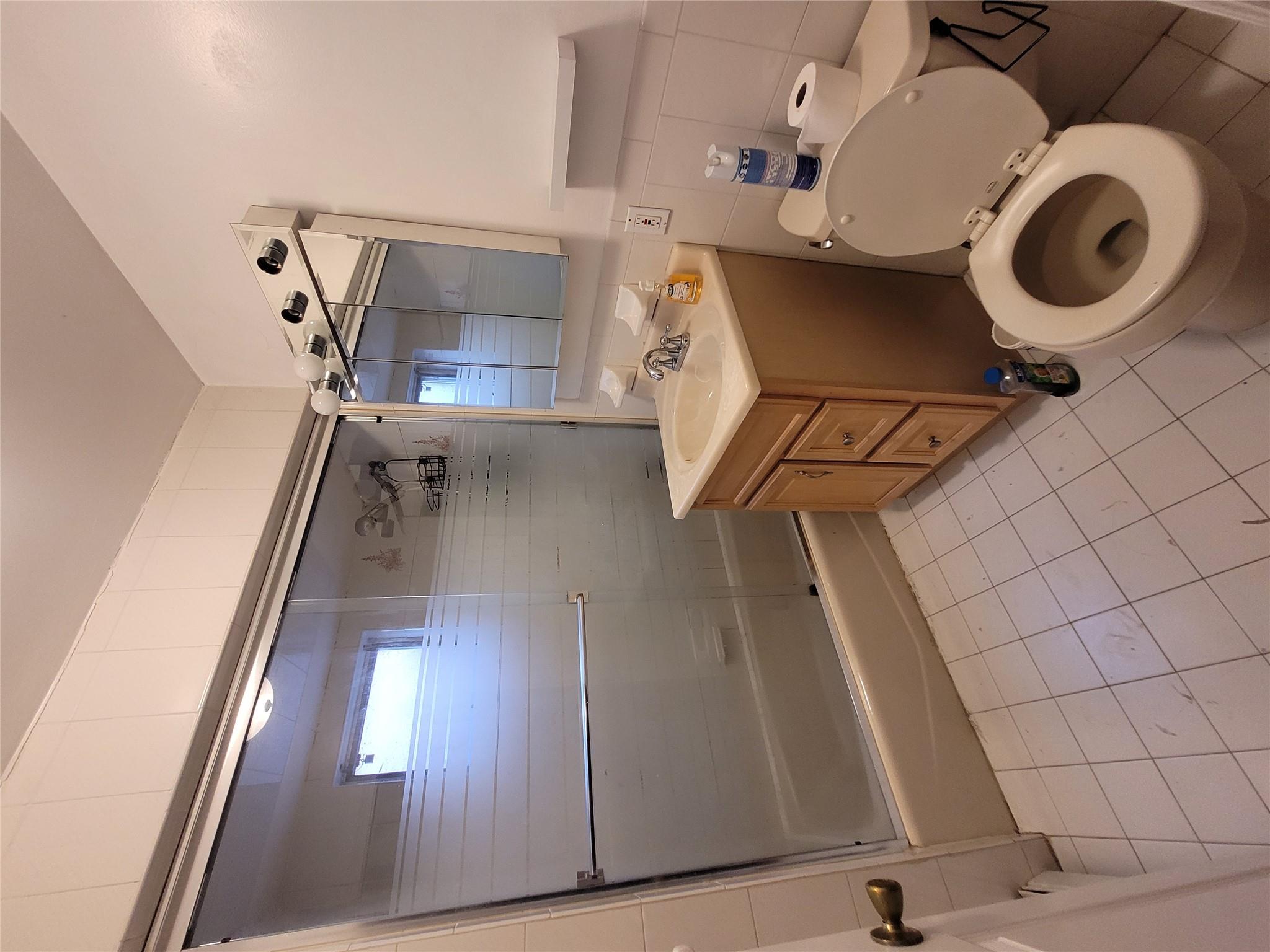 1124 67th Street, Unit A3 Brooklyn, NY 11219 - Photo 10 of 20 Full bathroom featuring tile walls, bath / shower combo with glass door, toilet, tile patterned floors, and vanity