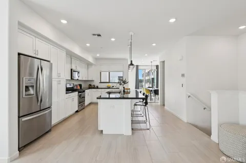 a kitchen with stainless steel appliances kitchen island granite countertop a refrigerator a sink dishwasher a stove and white cabinets with wooden floor