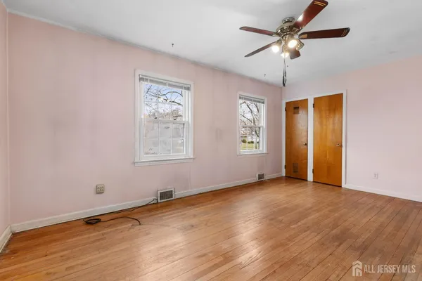 an empty room with wooden floor chandelier fan and windows