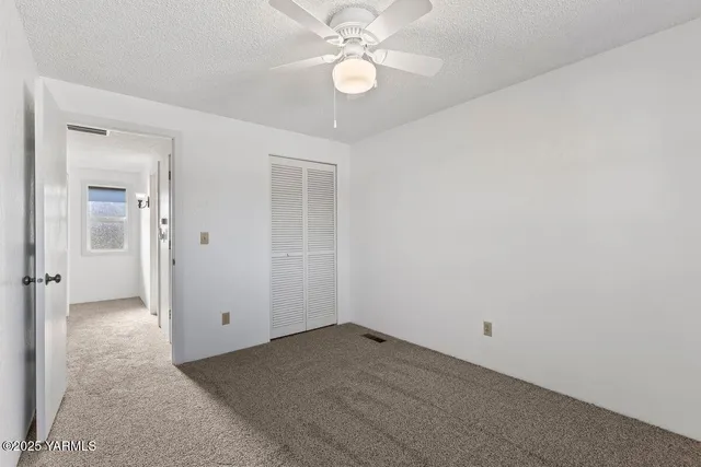 an empty room with chandelier fan and closet area