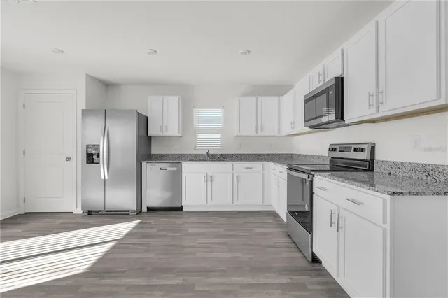 a kitchen with stainless steel appliances granite countertop a refrigerator sink and white cabinets