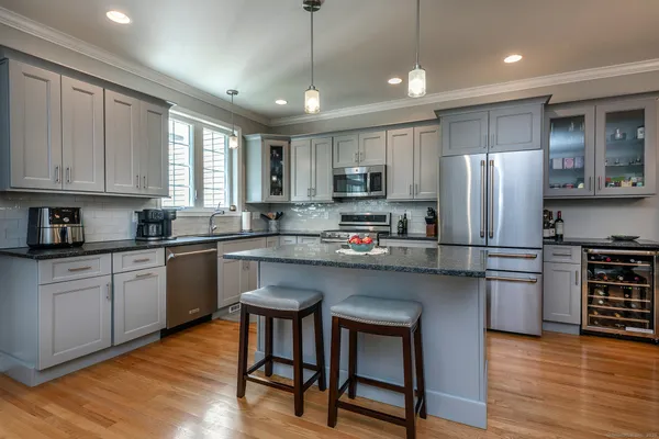 a kitchen with kitchen island granite countertop a refrigerator a stove a sink and white cabinets with wooden floor