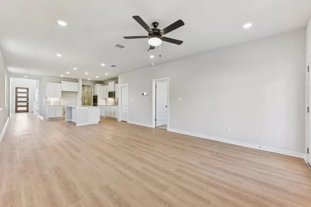 an empty room with wooden floor a ceiling fan and kitchen view