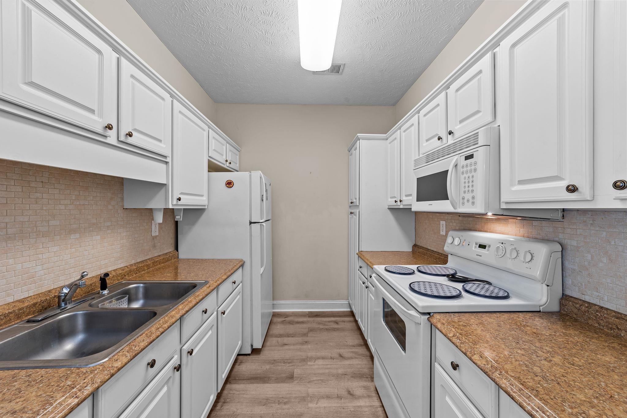 120 Fountain Pointe Lane, Unit 103 Myrtle Beach, SC 29579 - Photo 10 of 26 Kitchen with white appliances, white cabinets, tasteful backsplash, a textured ceiling, and light wood finished floors