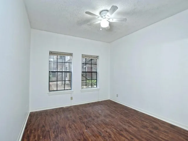 an empty room with wooden floor chandelier fan and windows