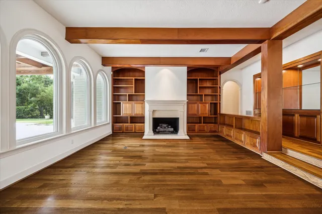 a view of an empty room with wooden floor fireplace and a window