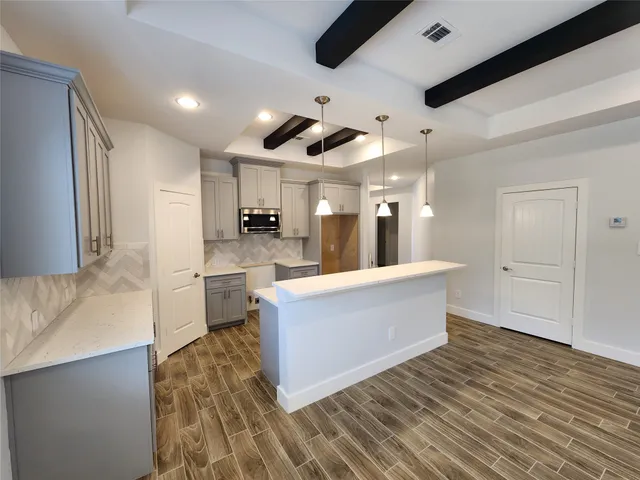 a large kitchen with stainless steel appliances a large counter top space wooden floor and a ceiling fan