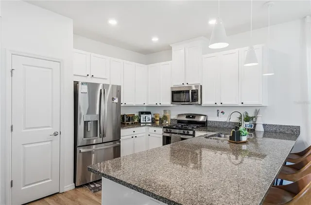 a kitchen with stainless steel appliances granite countertop a refrigerator a stove a sink a microwave and white cabinets