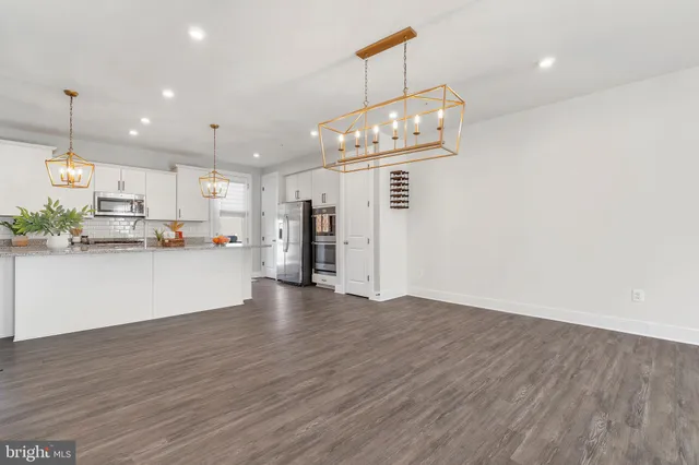 a kitchen with stainless steel appliances granite countertop a stove a refrigerator a sink and white cabinets with wooden floor