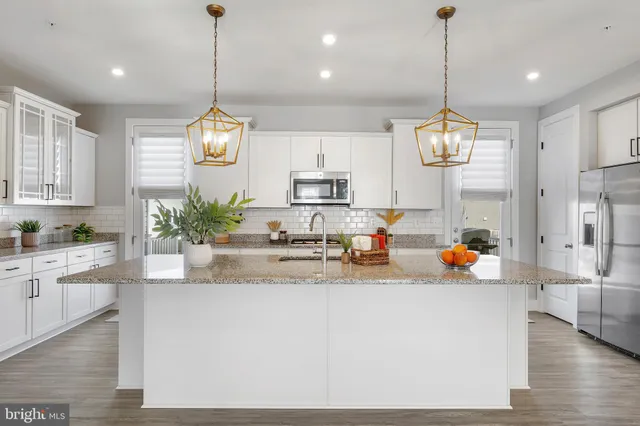 a kitchen with stainless steel appliances kitchen island granite countertop a refrigerator a sink a stove and a wooden floors