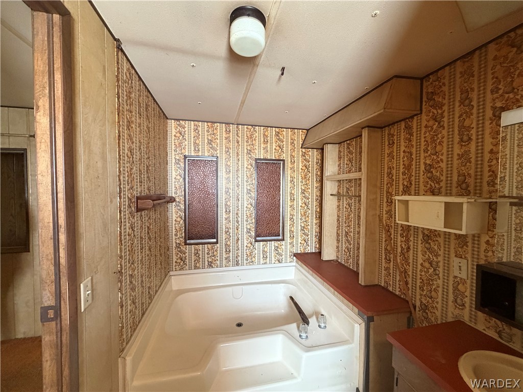 1666 Talc Road Bullhead City, AZ 86442 - Photo 27 of 61 Bathroom featuring a built-in tub, patterned wallpaper, wall-mounted shelving, and a vanity with a red countertop and integrated sink