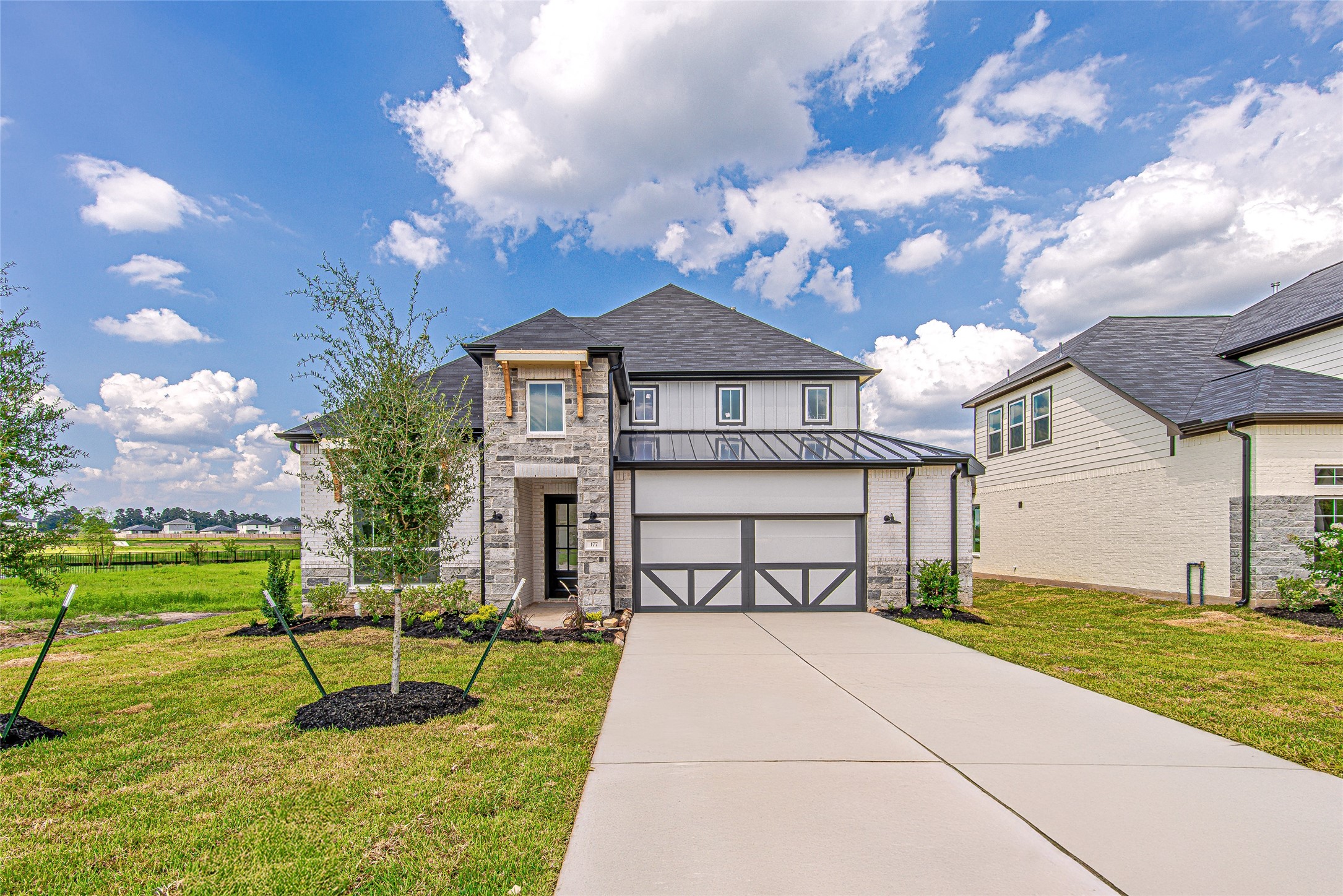 Modern curb appeal meets timeless design with this striking front elevation featuring stone accents, a dark metal awning, and charming board-and-batten garage doors.