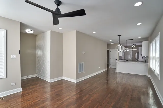 a view of an empty room and kitchen with wooden floor