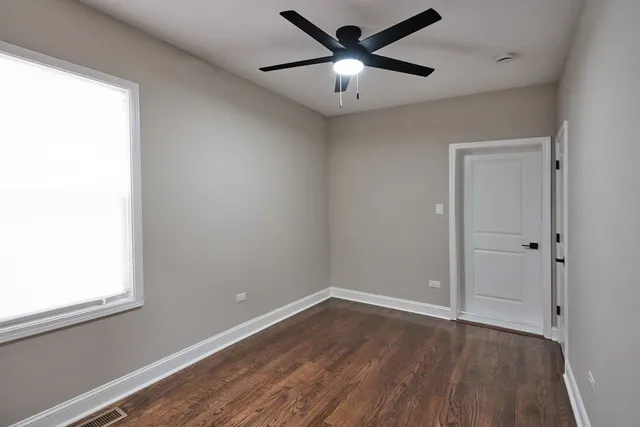 an empty room with wooden floor fan and windows