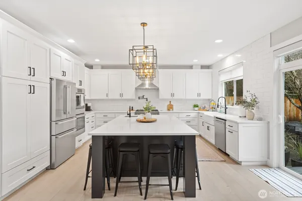 a kitchen with stainless steel appliances granite countertop a refrigerator a sink dishwasher a stove a dining table and chairs with wooden floor