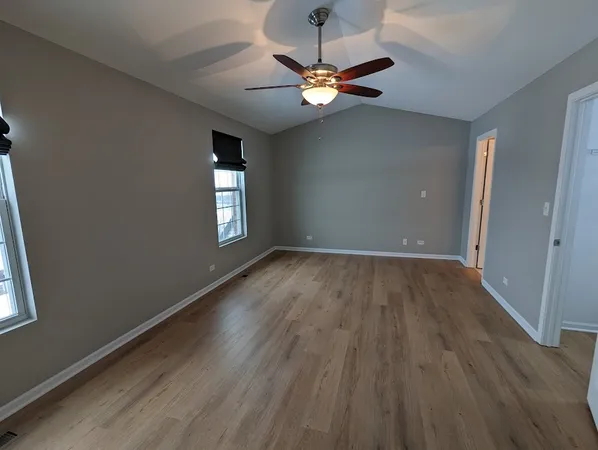 an empty room with wooden floor chandelier fan and windows