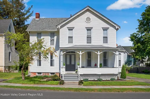 a view of a white house with a small yard plants and large trees