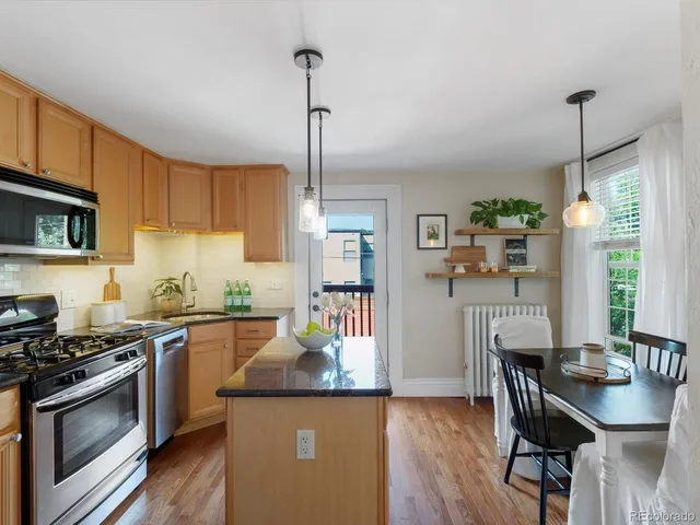 a kitchen with stainless steel appliances granite countertop a stove top oven a sink dishwasher a dining table and chairs with wooden floor