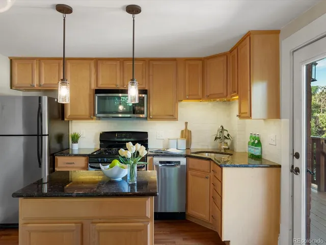 a kitchen with stainless steel appliances granite countertop a refrigerator a sink dishwasher a stove and a dining table with wooden floor