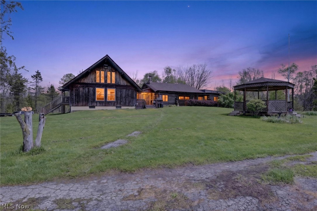 Expansive property featuring a rustic-style home with dark wood siding, a prominent A-frame section with multi-pane windows, and a detached gazebo with a lattice roof