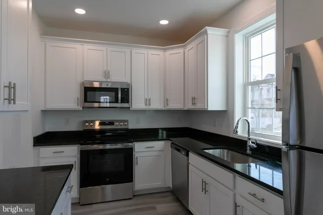 a kitchen with granite countertop white cabinets sink and stainless steel appliances
