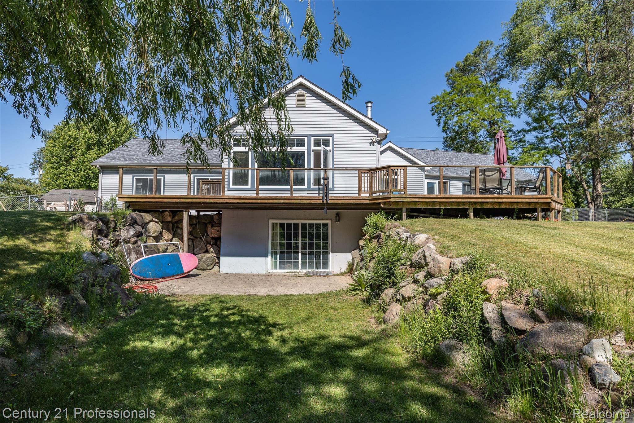 3251 Mann Road Clarkston, MI 48346 - Photo 2 of 40 Rear exterior featuring a spacious wood deck, light gray siding, multiple windows, and a sliding glass door on the lower level