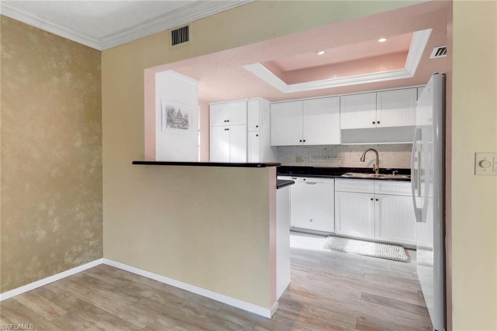 1155 Sandpiper Street, Unit D4 Naples, FL 34102 - Photo 30 of 39 Kitchen with white appliances, light wood-type flooring, white cabinetry, tasteful backsplash, and dark countertops