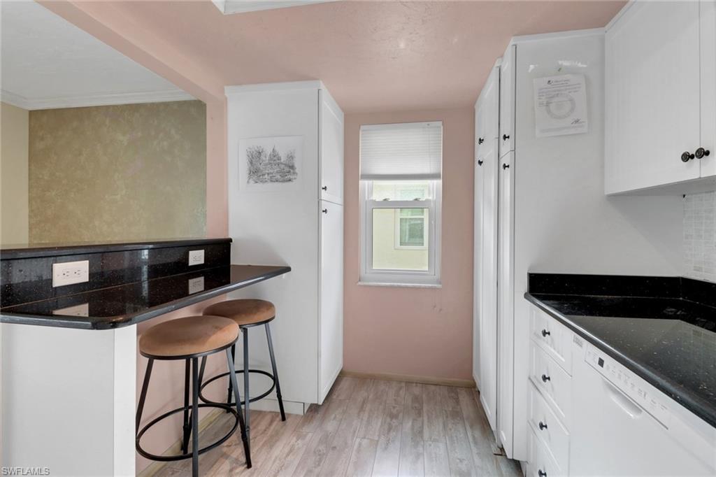 1155 Sandpiper Street, Unit D4 Naples, FL 34102 - Photo 8 of 39 Kitchen with light wood-style flooring, white dishwasher, white cabinetry, a kitchen bar, and crown molding