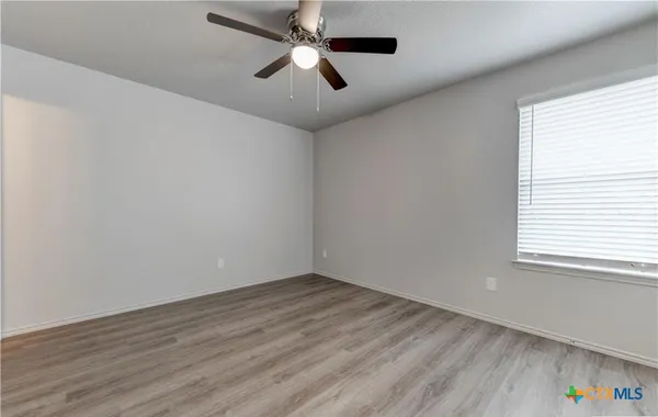 an empty room with wooden floor ceiling fan and windows
