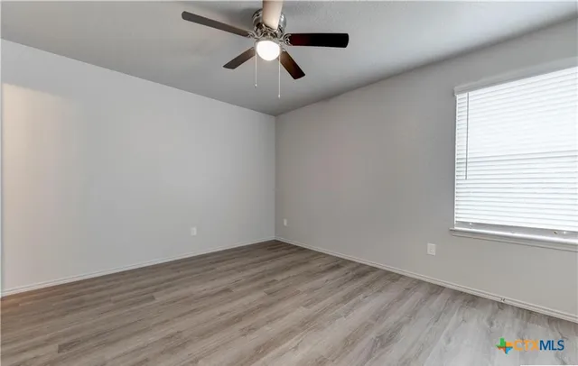 an empty room with wooden floor ceiling fan and windows