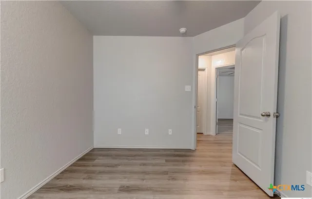 a view of an empty room with wooden floor and a hallway