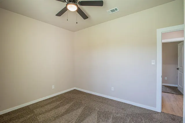an empty room with a ceiling fan and carpet
