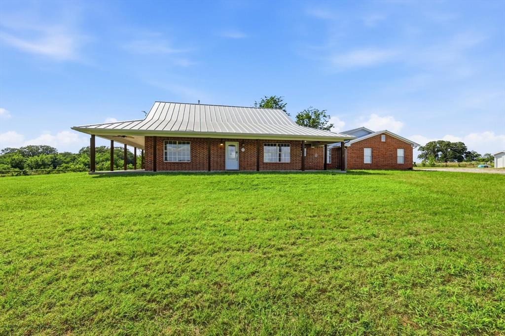 12190 Bell Road Pilot Point, TX 76258 - Photo 2 of 39 Brick exterior residence featuring a corrugated metal roof, a full-length covered porch with dark support columns, and multiple windows