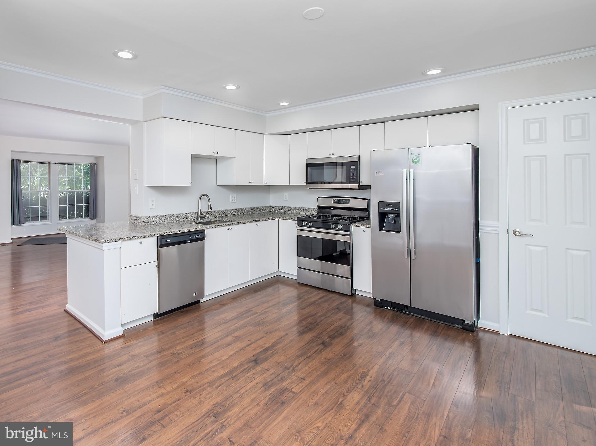 a kitchen with stainless steel appliances granite countertop a refrigerator a sink dishwasher a stove top oven a refrigerator with grey cabinets with wooden floor and cabinets