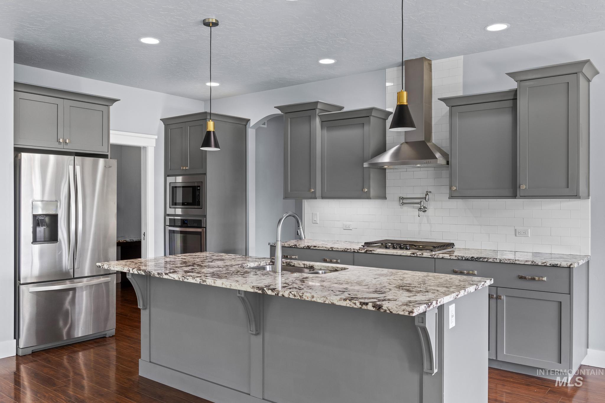 2681 East Rhyolite Court Nampa, ID 83686 - Photo 12 of 48 Kitchen featuring a central island with a sink, grey shaker-style cabinetry, stainless steel appliances, white subway tile backsplash, and wood-finish flooring