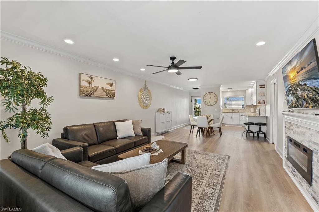 1020 Palm View Drive, Unit C302 Naples, FL 34110 - Photo 1 of 19 Living area featuring a glass covered fireplace, ceiling fan, light wood-style floors, crown molding, and recessed lighting
