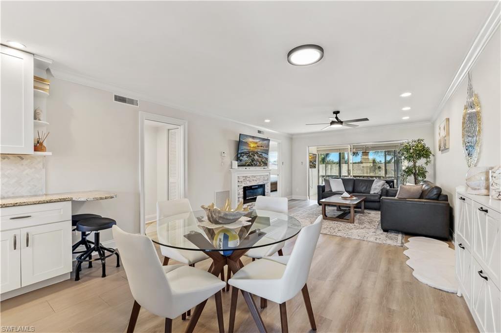 1020 Palm View Drive, Unit C302 Naples, FL 34110 - Photo 9 of 19 Dining area with crown molding, a glass covered fireplace, light wood-style floors, recessed lighting, and ceiling fan