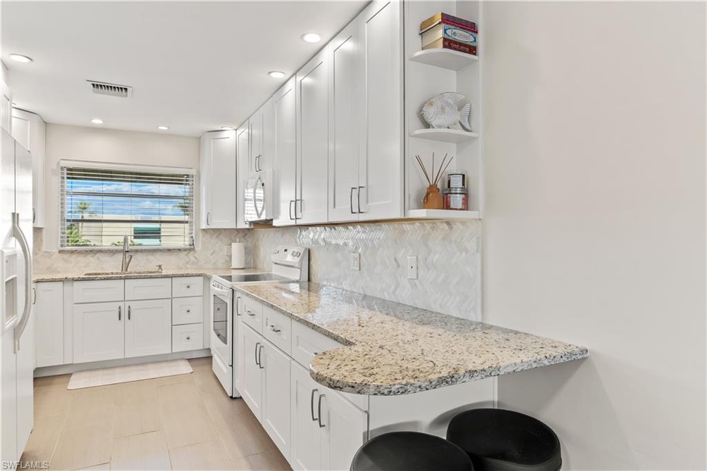 1020 Palm View Drive, Unit C302 Naples, FL 34110 - Photo 10 of 19 Kitchen with open shelves, light stone countertops, white appliances, white cabinetry, and a kitchen bar