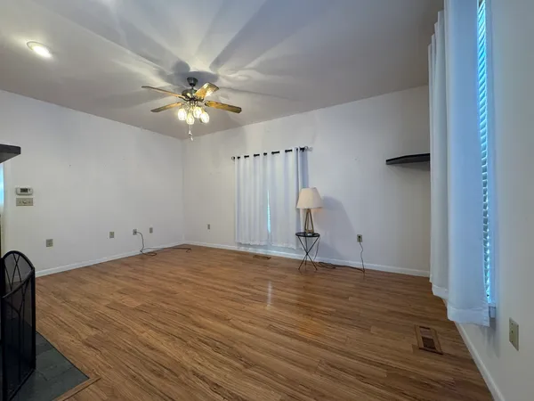 an empty room with wooden floor fan and windows
