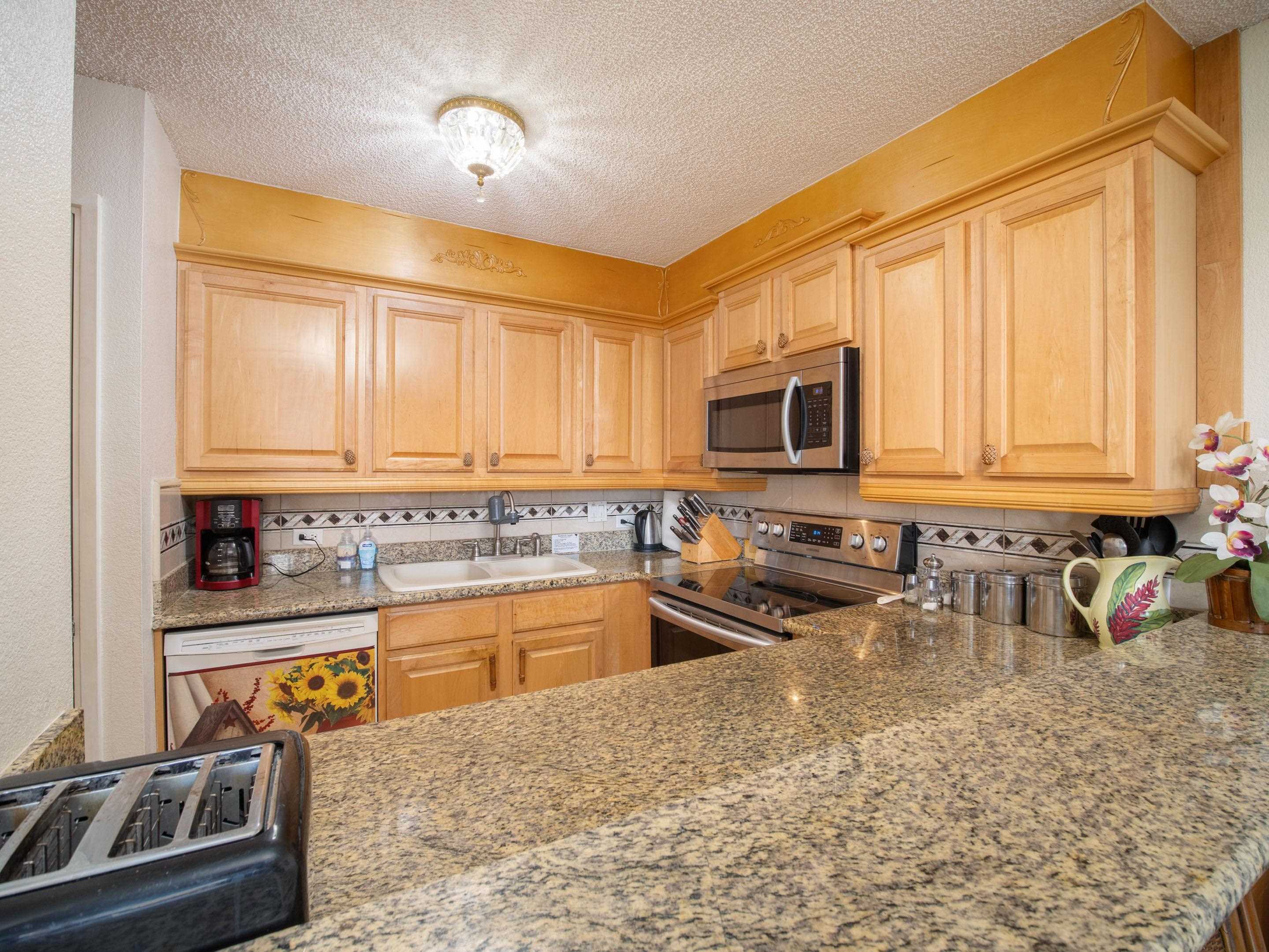 2695 South Kihei Road, Unit 7204 Kihei, HI 96753 - Photo 8 of 32 a kitchen with stainless steel appliances granite countertop a stove top oven a sink a dining table and chairs with wooden floor