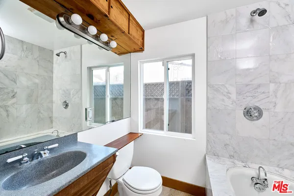 a bathroom with a granite countertop sink a toilet a mirror and shower