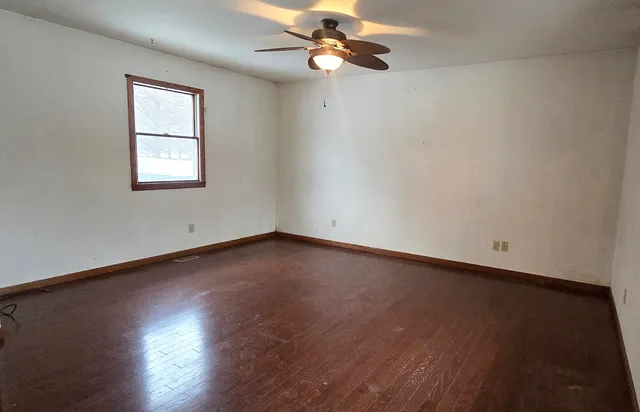 an empty room with wooden floor chandelier fan and windows