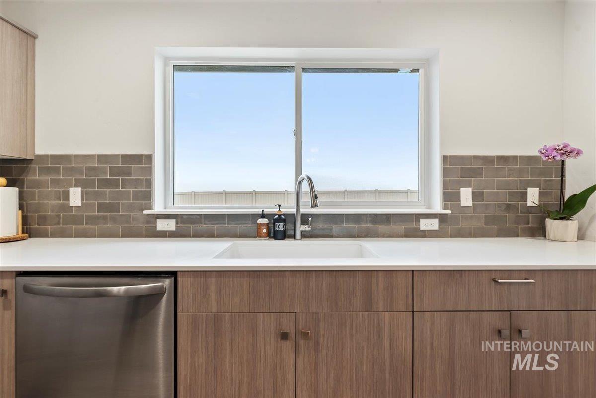 4086 North Kithnos Avenue Meridian, ID 83646 - Photo 11 of 29 Kitchen featuring stainless steel dishwasher, brown cabinetry, plenty of natural light, and tasteful backsplash