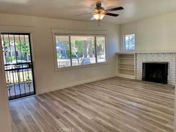 a view of an empty room with wooden floor fireplace and a window