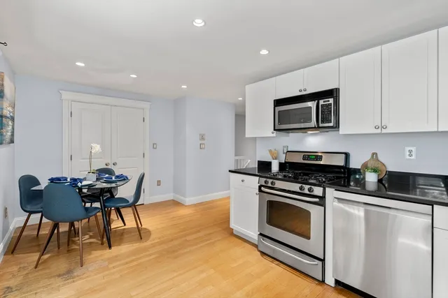 a kitchen with stainless steel appliances kitchen island granite countertop a stove a sink a microwave a dining table and chairs with wooden floor