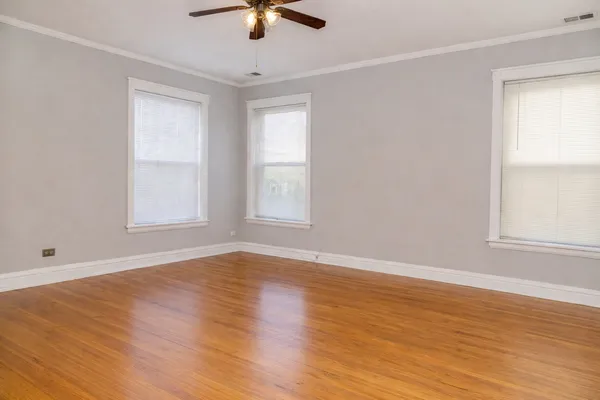 an empty room with wooden floor fan and windows