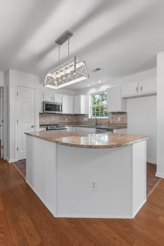 a view of kitchen with granite countertop stainless steel appliances stove and white cabinets