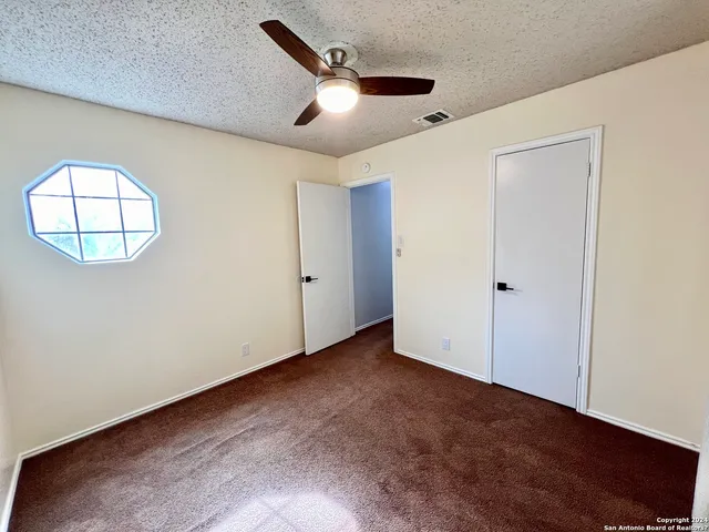 an empty room with a chandelier fan and wooden floor